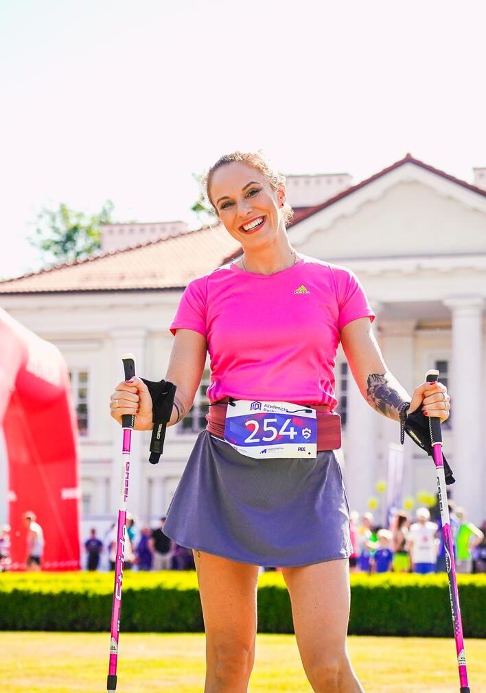 Kobieta z kijkami do Nordic Walking pozuje do zdjęcia przed Pałacem Ogińskich.